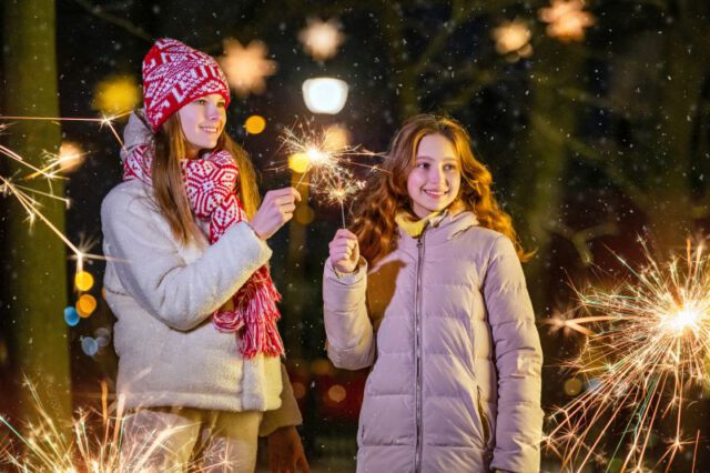 A company of cheerful teenage girls walking through the night party city during a snowfall, burning sparklers